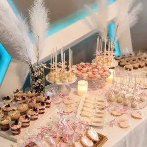 Mesa de postres de boda con macarons rosas, cake pops blancos y decoración de plumas y velas.