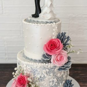 Tarta de boda con detalles de encaje azul, rosas fucsia y figura divertida de novia atrapando al novio.