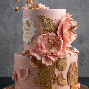 Tarta de aniversario de dos pisos rosa pastel decorada con grandes flores de oro comestible y topper geométrico "Habib 20 years Anniversary".