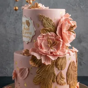 Tarta de aniversario de dos pisos rosa pastel decorada con grandes flores de oro comestible y topper geométrico "Habib 20 years Anniversary".